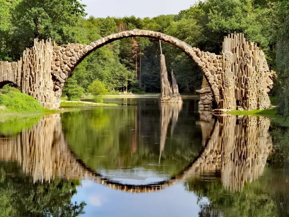 Pont de pierre se reflétant dans un lac, au cœur de la forêt